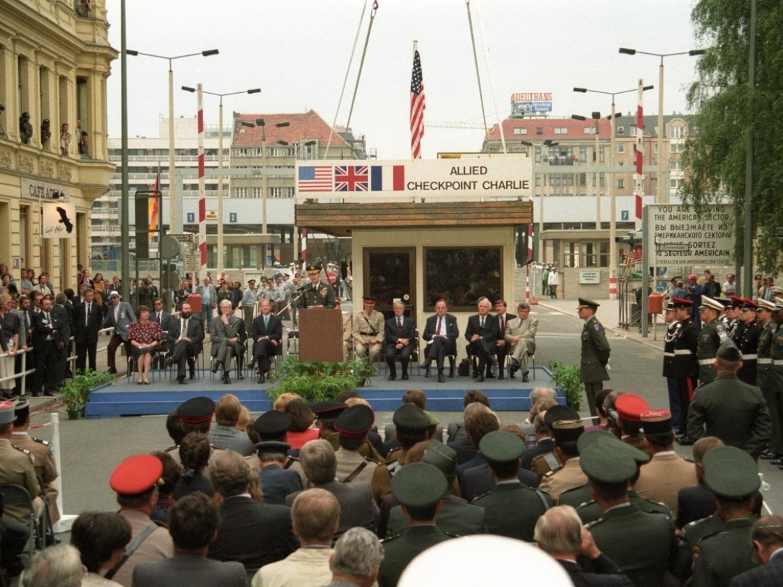 Das Kontrollhäuschen am Checkpoint Charlie wird mit einem Kran gehoben - vorne sitzen Gäste und Außenminister