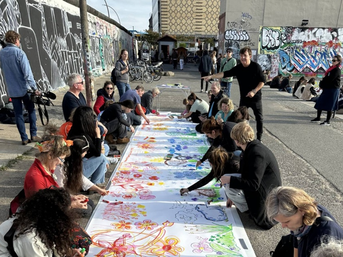 Menschen malen vor der East Side Gallery zusammen auf dem Boden auf einer großen Leinwand
